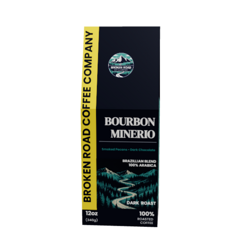 A 12oz box of Broken Road Coffee Company Bourbon Minerio Dark Roast coffee, featuring a dark navy blue and black design with a bright yellow vertical banner on the left and a scenic mountain graphic.