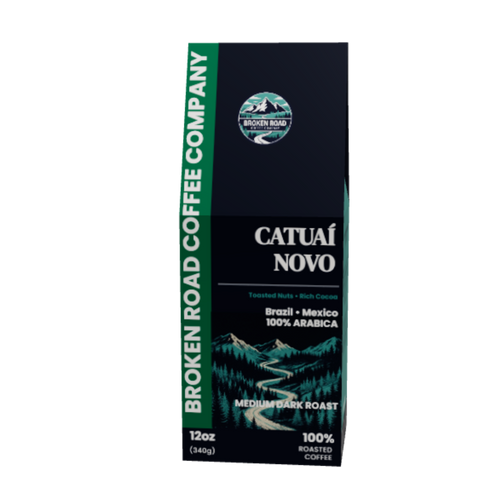 A 12oz package of Broken Road Coffee Company Catual Novo Medium Dark Roast coffee, featuring a dark navy blue box with green accents and a scenic mountain illustration.