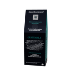 A tall, narrow black coffee bag package with teal and white text, photographed on a plain white background. The front prominently reads 'GUATEMALA' and includes descriptive coffee text and a small QR code.