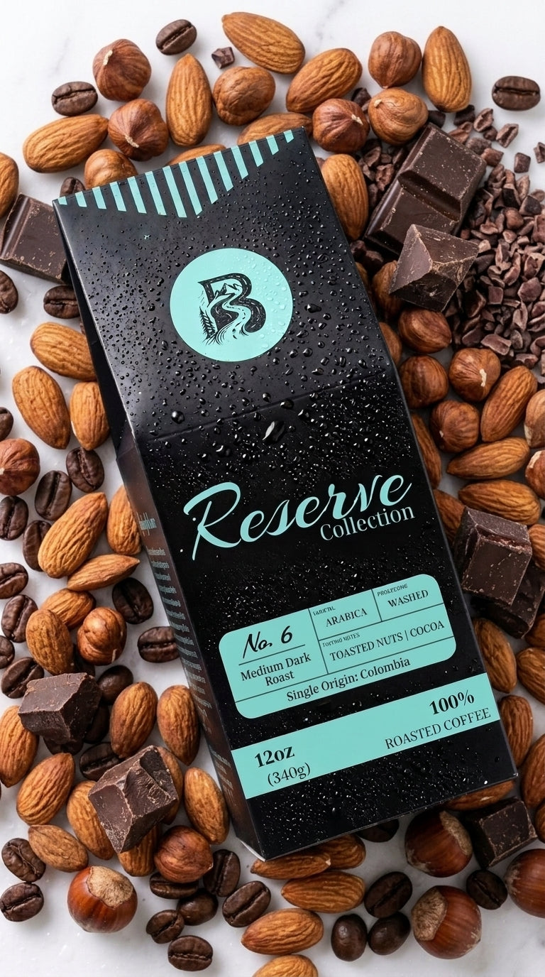 A chocolate bar package from Reserve Collection lies diagonally on a white marble surface, surrounded by whole almonds, dark chocolate chunks, and coffee beans. The package is black with teal accents and white lettering.
