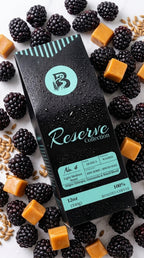 A black coffee bag from the Reserve Collection is surrounded by fresh blackberries, caramel cubes, and whole flaxseeds on a white background.